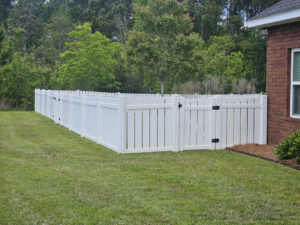 a white vinyl fence in a well maintained yard surrounded by greenery and grass