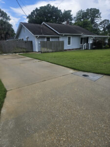 aquatech pressure washing cleaning a concrete driveway surrounded by grass and a wooden fence