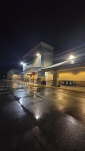 A brightly lit storefront at night with freshly pressure washed sidewalks and pavement glistening under the lights