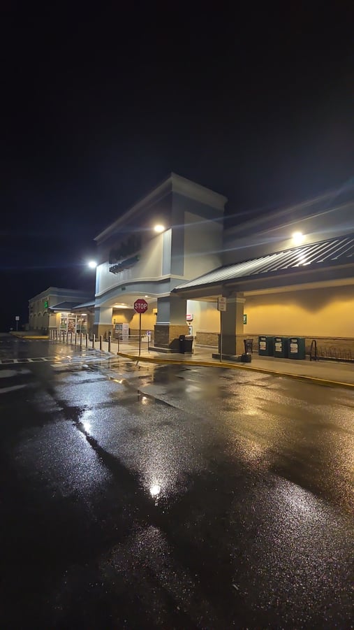 A brightly lit storefront at night with freshly pressure washed sidewalks and pavement glistening under the lights