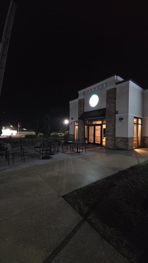 A freshly pressure washed concrete sidewalk and patio area outside a well-lit commercial storefront at night