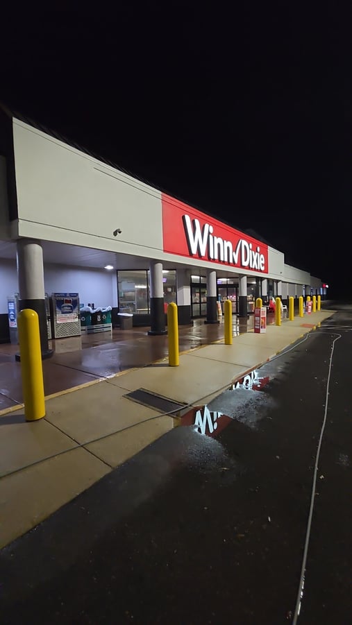 Clean, freshly pressure washed concrete walkway at the entrance of a Winn-Dixie store at night, with wet surfaces reflecting the storefront lights